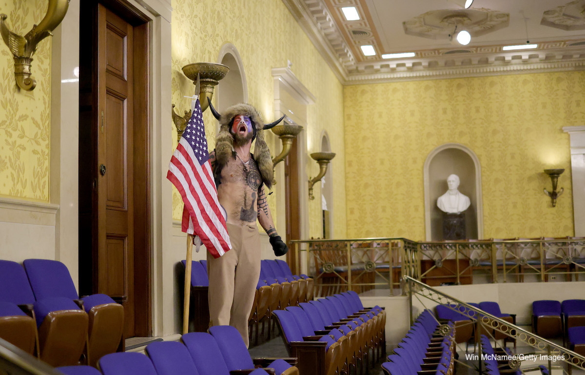 protester in horned hat with American flag yelling in Capitol building chambers